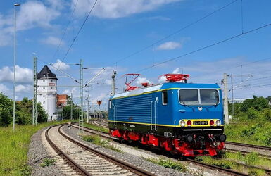 einzelne blaue Elektrolok BR243 auf der Strecke und im Hintergrund ist ein turmähnliches Stellwerkhaus zu sehen