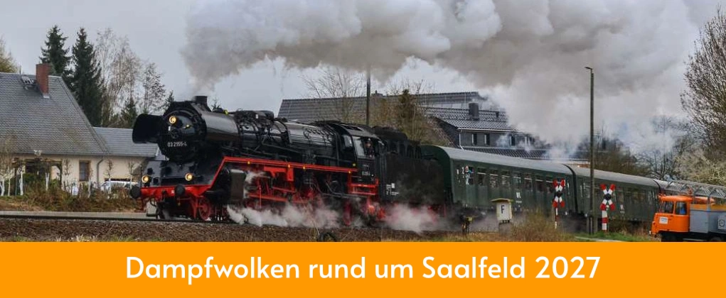 Dampflok Sonderzug fährt unter Volldampf an beschranktem Bahnübergang vorbei